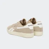 Championes Reebok modelo Court Retro, confeccionados en gamuza color beige con detalles en blanco y suela de goma color marfil. Presentan el logo de la marca en el lateral y en el talón.