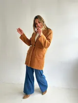 Abrigo estilo sastrero de textura tipo bouclé en color camel, con cierre frontal de un botón, solapas clásicas y bolsillos frontales tipo plaqué.