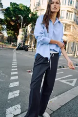 Camisa básica de algodón con cuello solapa, escote en pico y cierre frontal con botones. Presenta mangas largas con puños abotonados y bajo redondeado.