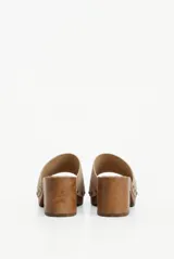 Zueco de taco medio con base de madera, capellada de gamuza beige y detalle de tachas metálicas en los laterales.