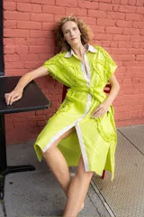 Vestido camisero color verde lima con lurex, cuello camisero blanco, cierre frontal con botones blancos y lazo en la cintura. Presenta volados en el frente y en el ruedo.