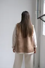 Chaleco de gamuza color beige con interior y detalles de corderito color crudo. Presenta solapas amplias, bolsillos frontales aplicados y diseño sin mangas.