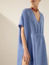 Túnica blanca de lino con corte asimétrico, mangas cortas y escote en V con pespuntes.