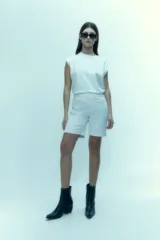 Bermuda de denim blanco con diseño clásico de cinco bolsillos, cierre frontal con botón y bragueta, y corte recto a la altura de la rodilla.