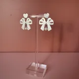Par de aros colgantes blancos con forma de moño y corazón, con una perla colgando.