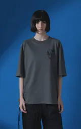 Remera de manga corta con cuello redondo y calce oversize, color gris oscuro. Presenta una estampa frontal con diseño gráfico de un escorpión y una rosa, junto con texto tipográfico.