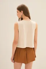 Musculosa color crema con estampado de mariposa y manos en dorado, escote en V con tachas y corte holgado.