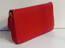 Billetera rectangular de cuero color beige con cierre perimetral y tirador de cuero. Cuenta con múltiples compartimentos internos para tarjetas, documentos y billetes, además de un bolsillo interno con cierre para monedas y forro textil en color rojo.