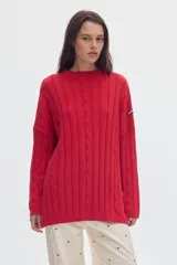 Buzo tejido de algodón color rojo, con cuello alto, diseño oversized, patrón de ochos verticales, pequeños tajos laterales y parche distintivo en la manga.