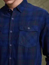 Camisa de pana color azul marino, con mangas largas, cuello clásico y dos bolsillos frontales con solapa y botón.