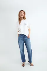 Camiseta de corte oversize, color blanco, con cuello redondo, mangas cortas y estampa botánica pequeña en el pecho.