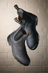 Botas tipo chelsea Blundstone modelo #1910, confeccionadas en gamuza gris repelente al agua. Presentan elásticos laterales negros, tiradores en la parte superior y suela de TPU antideslizante con entresuela acolchada para mayor confort.