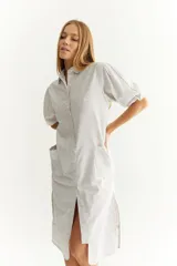 Vestido camisero midi de lino a rayas verticales grises y blancas, con cuello camisero, mangas cortas abullonadas, cierre frontal con botones y bolsillos laterales.