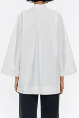 Camisa blanca de algodón, de corte línea A, con cuello mao con lazo a modo de cierre y manga larga ancha con pespunte bordado en puños.