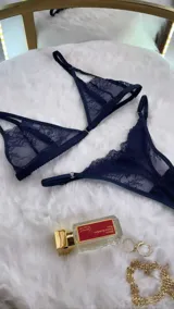 Set de lencería de cuatro piezas en encaje azul marino. Incluye bralette con breteles regulables y broche frontal, tanga colaless regulable con entrepierna de algodón, y chaleco con portaligas integrado con ligas regulables.