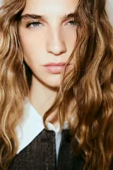 Chaleco largo de vestir, color marrón oscuro jaspeado, con cuello redondo, cierre frontal de botones y bolsillos ribeteados. Presenta un corte entallado y forro interior.