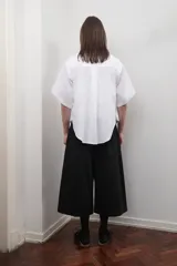 Camisa blanca oversize de popelina de algodón, con cuello clásico, manga corta amplia, bolsillo frontal y canesú en la espalda con pliegue central.