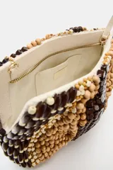 Bolso tipo pouch confeccionado completamente con cuentas de madera en tonos marrón, beige y tostado, formando un patrón abstracto. Cuenta con una correa fina de cadena dorada desmontable y cierre superior con cremallera.