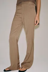 Pantalón flare de tiro medio, confeccionado en mezcla de viscosa y lino, con diseño de rayas verticales en tono beige. Cuenta con bolsillos delanteros y bajo acabado en línea evasé. Cierre frontal con cremallera, botón y ganchos metálicos.