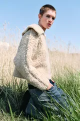 Chaqueta de punto bouclé color crudo, con cuello de solapa grande, manga larga y cierre frontal con cremallera.