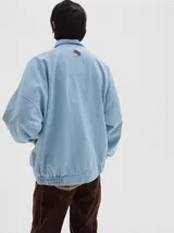 Campera de denim estilo deportivo con diseño de paneles en tonos azul claro y blanco, cuello alto, cierre frontal y bolsillos laterales con cierre. Presenta corte oversized con puños y cintura elásticos.