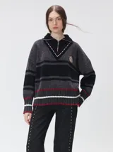 Pullover de punto con textura aterciopelada, diseño oversize, cuello polo con cierre frontal parcial y detalles de pespuntes en contraste. Presenta rayas horizontales en tonos tierra y un parche bordado con la letra M en el pecho.