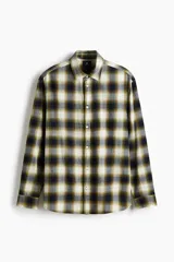 Camisa de franela de algodón suave con cuello inglés, cierre frontal de botones, mangas largas con puños abotonados y bajo redondeado. Presenta un diseño a cuadros en tonos oscuros y amarillentos.