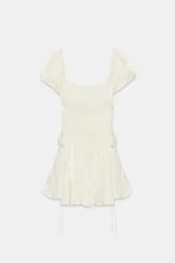 Vestido mini de tejido jacquard color blanco crudo, con escote cuadrado, mangas cortas abullonadas y detalles de lazadas en los laterales.