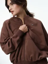 Campera deportiva color bordó con cuello tipo bomber, cierre frontal completo y mangas raglán. Presenta puños, cuello y ruedo acanalados, además de bolsillos frontales.