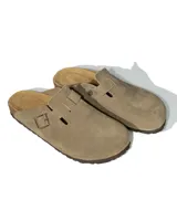 Zuecos de gamuza color beige con diseño de punta cerrada y ajuste lateral mediante tira con hebilla metálica grabada. Presentan una plantilla anatómica de corcho y látex, con suela de goma antideslizante.