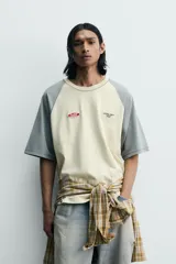 Camiseta de corte relajado con mangas ranglán en color gris y cuerpo en color beige. Presenta cuello redondo, costuras a contraste y detalles de parches y bordados en el pecho.