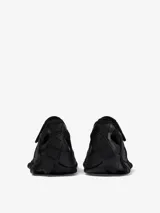 Zapatilla urbana de diseño vanguardista en color negro, con estructura de malla y superposiciones de paneles de goma texturizados. Presenta cierre con tiras autoadherentes y suela robusta con diseño ergonómico.