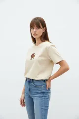 Remera cropped de algodón color beige, de corte holgado, con cuello a la base, manga corta y pequeño estampado en el pecho.