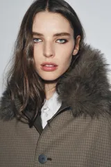 Trench reversible de corte recto con cuello de solapa y aplicación de pelo sintético extraíble. Presenta cierre frontal con botones, manga larga y bolsillos laterales ocultos en las costuras.