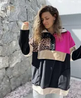 Buzo de estilo canguro con diseño color block que combina paneles en negro, fucsia, beige y un estampado de leopardo. Presenta cuello con cierre de botones a presión y un bolsillo frontal tipo canguro.