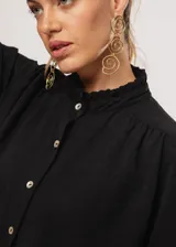 Camisa negra de cuello redondo con frunces y mangas largas con puños abiertos.