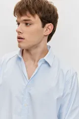 Camisa de manga larga con cierre frontal de botones y cuello clásico, color celeste con sutiles rayas verticales.