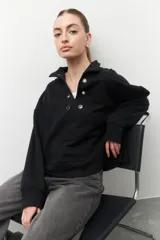 Buzo marrón de algodón con cuello alto y apliques de argollas metálicas.