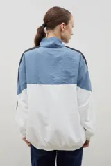 Campera de tela avión con diseño color block en negro y verde, con detalles de franjas blancas en las mangas. Presenta cierre frontal completo, cuello alto, puños y ruedo elásticos, y logo bordado en el pecho.