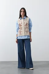 Chaleco tejido color marrón con bordados artesanales de motivos florales y geométricos en color crema. Presenta cuello redondo, cierre frontal con botones y diseño sin mangas.