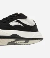 Championes urbanos de hombre, modelo street, color negro y blanco. Presenta capellada de material sintético (PU) con recortes, puntera redonda, cordones negros y paneles de malla blanca para ventilación. Posee una suela gruesa (bold) de color blanco y negro.