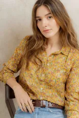 Camisa de corte clásico con cuello camisero y cierre frontal de botones, confeccionada en tela con estampado floreado en tonos amarillos, rosas y blancos.