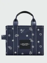 Cartera tipo tote bag de lona azul marino con estampado de motivos blancos y letras blancas bordadas en el frente. Cuenta con doble asa superior y cierre superior con cremallera.
