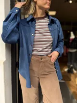 Sobrecamisa de gamuza con cuello clásico, cierre frontal con botones metálicos y mangas largas con puños abotonados. Presenta un diseño estructurado con corte recto y largo a la cadera.