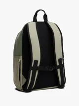 Mochila de nailon color verde oliva, con diseño liso y paneles texturizados. Presenta un compartimento principal con doble cremallera, un bolsillo frontal con cremallera y un parche con el logo de Tommy Jeans en la parte inferior. Las correas y el asa superior son negras.