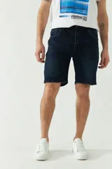 Bermuda de jean azul oscuro con bolsillos delanteros y traseros, cierre con cremallera y trabillas para cinturón.