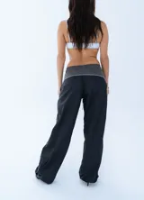 Pantalon deportivo de estilo urbano, confeccionado en tela técnica, con cintura elástica ajustable mediante cordón. Presenta un diseño bicolor en negro y gris oscuro con líneas laterales en contraste.
