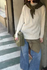 Sweater de punto color beige melange, de corte holgado, con cuello alto, mangas largas y costura central visible en el frente.