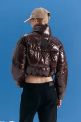 Campera puffer corta de acabado brillante en color marrón oscuro, con cuello alto, cierre frontal y diseño acolchado.