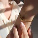 Pulsera dorada de eslabones finos con dije redondo liso.